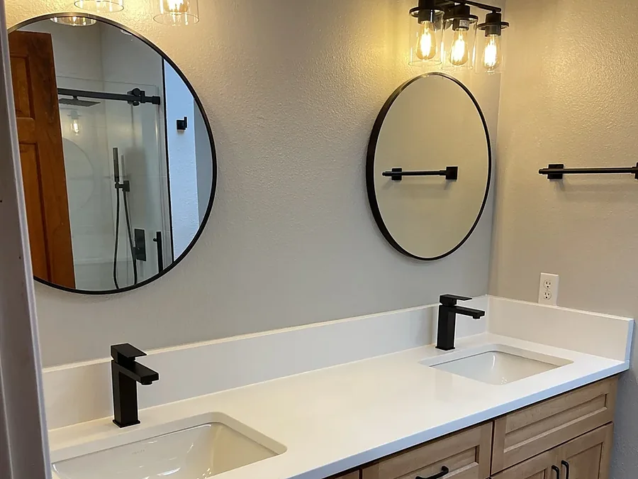 Vanity with wood cabinetry, quartz top, round mirrors and sconce lighting